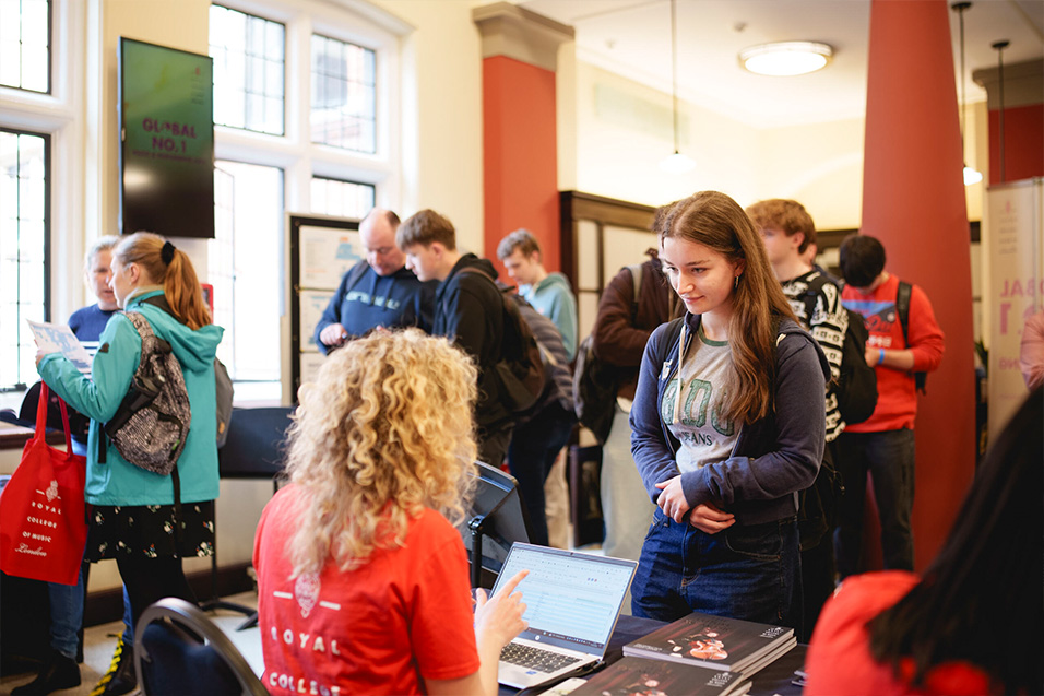 A young woman stands at a table, engaging with a staff member wearing a red shirt that reads 